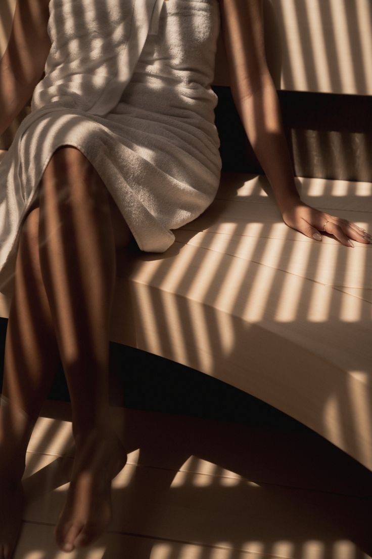 Soft sunlight through sauna slats falls across a person resting in a towel.
